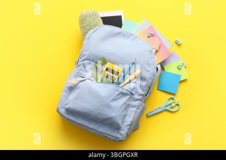 Blue school backpack with different stationery supplies and modern tablet computer on yellow background Stock Photo
