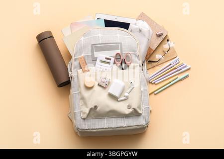 Stylish school backpack with different stationery supplies, thermos and modern tablet computer on beige background Stock Photo
