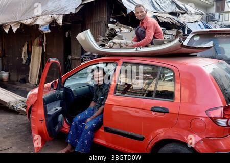 An Indian man sits on the roof of a junk car working on a discarded car part; at Chor Bazaar (Thieves' Market), a second-hand market in Mumbai, India Stock Photo