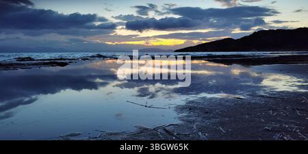 A peaceful coastal scene at sunrise on Marikes Beach in Rafina, Greece, where the still water reflects the colorful sky and dramatic clouds, blending Stock Photo