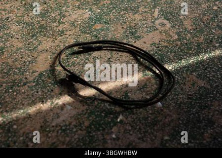 A coiled black braided USB cable lies on a terrazzo floor, illuminated by a dramatic shaft of light. Technology and connectivity concept Stock Photo