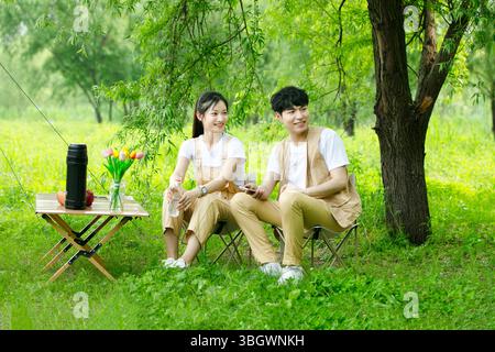 a young couple resting under a big tree while using their phones Stock Photo