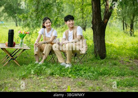 a young couple resting under a big tree while using their phones Stock Photo