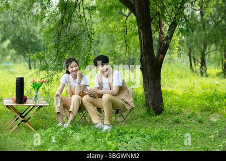 a young couple resting under a big tree while using their phones Stock Photo