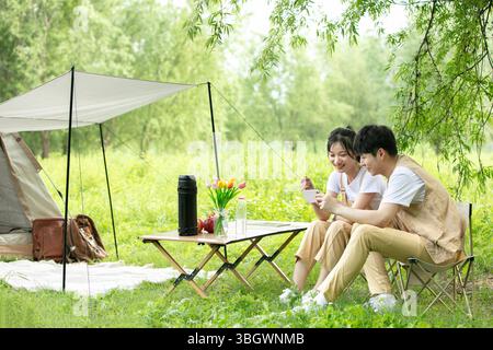a young couple resting under a big tree while using their phones Stock Photo