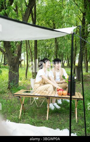 a young couple resting under a big tree while using their phones Stock Photo