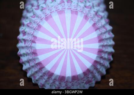 A close-up of a stack of pink and white cupcake liners. The liners feature a radial stripe pattern in the center, the liners are made from paper. Stock Photo