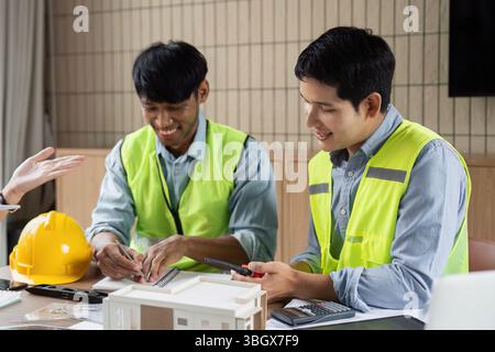 Green Tech and Collaboration. Two engineers discussing sustainable building designs with a model. Stock Photo