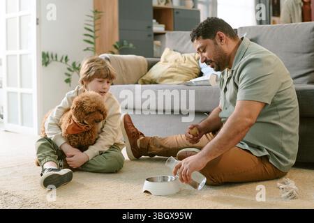 Caucasian Boy Holding Puppy Watching Middle Aged Man Preparing Dog Food Stock Photo