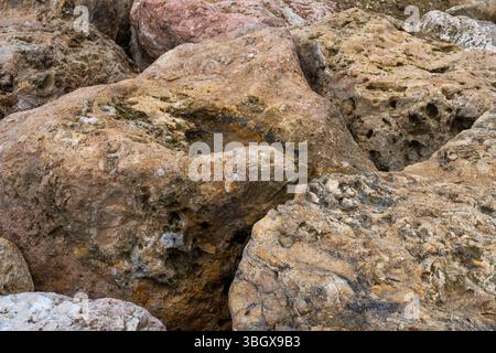 Pile of rocks on a beach. The rocks are brown and rough. The hole is small and dark Stock Photo