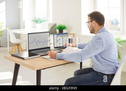 Focused business man analyzing financial data on desktop two laptop displays working on marketing  Stock Photo