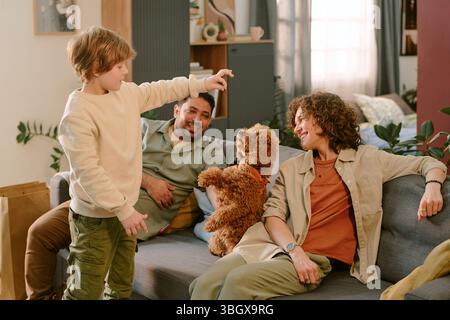 Caucasian Boy Playing with Puppy While Parents Smiling on Sofa at Home Stock Photo