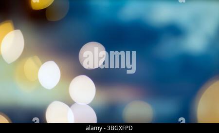 A blurry image featuring out-of-focus lights in shades of yellow and white against a deep blue background. The bokeh effect creates a soft, dreamy atm Stock Photo