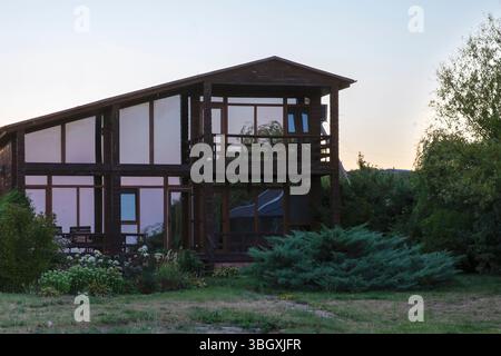 Contemporary wooden house with panoramic windows and garden in countryside. Greenery and flowers create cozy, eco-friendly atmosphere for real estate Stock Photo