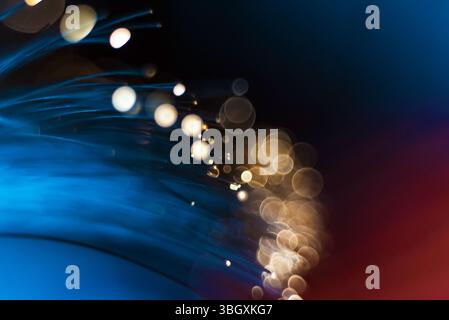 A close-up shot of illuminated fiber optic strands creating streaks of blue light with a bokeh effect of warm-toned circles in the background. Stock Photo