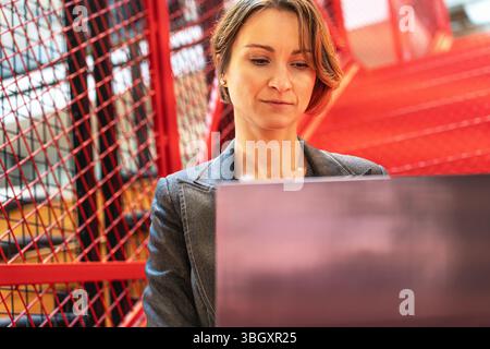 Female programmer working on code in modern office with industrial red stairs Stock Photo