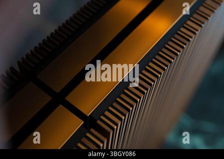 An abstract close-up shot reveals a textured metallic surface with repeating fins or grooves, highlighted by gold-toned flat sections and black accent Stock Photo