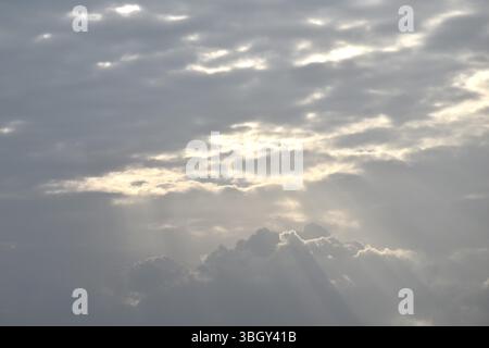 sun spreading light thourgh dark rain cloud floating on sky at sunset in evening Stock Photo
