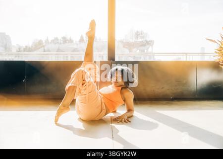 Woman lying on floor with one leg raised in sunlight Stock Photo