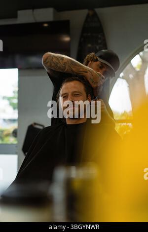 Tattooed barber trims smiling man's hair in modern barbershop Stock Photo