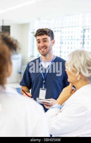 Young male nurse smiling and taking notes while talking with medical team in a hospital hallway Stock Photo