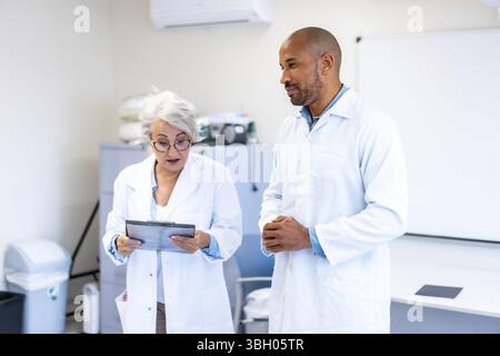 Two doctors engaged in a discussion over a patient chart inside a hospital room, collaborating on diagnosis and treatment strategies Stock Photo
