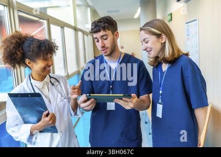 Doctors and nurses reviewing medical records on a tablet, collaborating on patient care in a hospital hallway Stock Photo