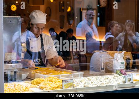 Florence, Italy - May 10th, 2025: Artisan chef preparing fresh pasta by hand in a shop window, as tourists look on from the street Stock Photo