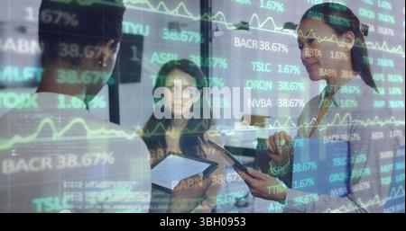 Analyzing three women reviewing data on tablet and smartphone in office, with stock chart overlay Stock Photo