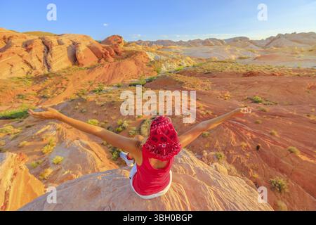 Freedom hiking woman at Valley of Fire State Park on top of Fire Wave at sunset. Happy hiker enjoying panoramic views of ribbons of red rock slice thr Stock Photo