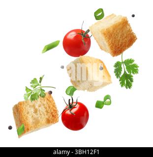 Delicious crispy croutons, tomatoes, peppercorns and herbs flying on white background Stock Photo