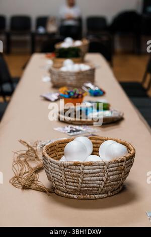 A long table is arranged for a creative workshop, displaying baskets filled with art supplies like colored eggs, twine, and craft materials, ready for Stock Photo