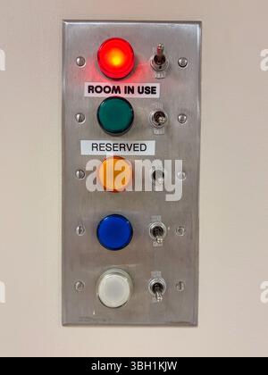 A wall-mounted metal panel features five colored lights with toggle switches, indicating room status Stock Photo