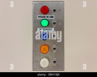 A wall-mounted metal panel features five colored lights with toggle switches, indicating room status Stock Photo
