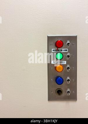 A wall-mounted metal panel features five colored lights with toggle switches, indicating room status Stock Photo