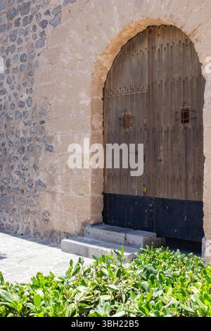 Rustic wood plank arched double doors leading into an old stone building Stock Photo