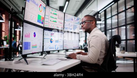 Diverse Young Man Analyzing Stock Charts On Computer Monitor Screen. Stock Photo
