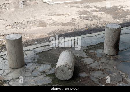 Three cement pillars are laying on the ground in front of a road. The scene is desolate and abandoned Stock Photo