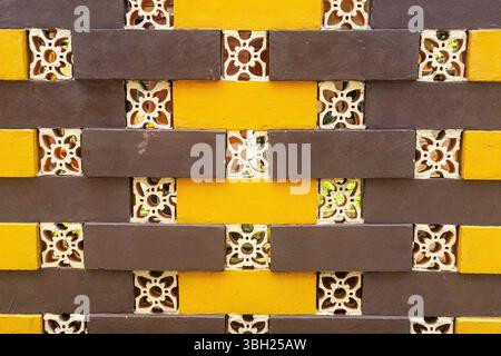 Brick wall with yellow and brown bricks and a pattern of flowers. The wall is made of bricks and has a yellow and brown color scheme Stock Photo