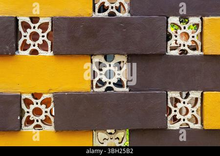 Brick wall with yellow and brown bricks and a pattern of flowers. The wall is made of bricks and has a yellow and brown color scheme Stock Photo