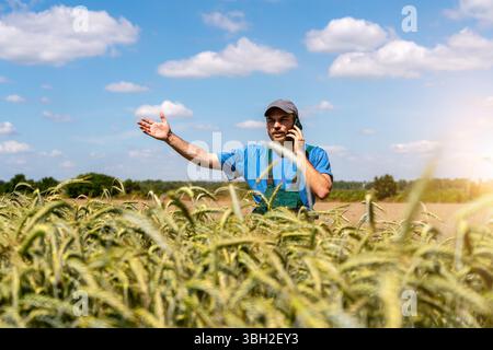 Male farmer gesturing and actively speaking on the phone while standing by cereal field in countryside. Stock Photo