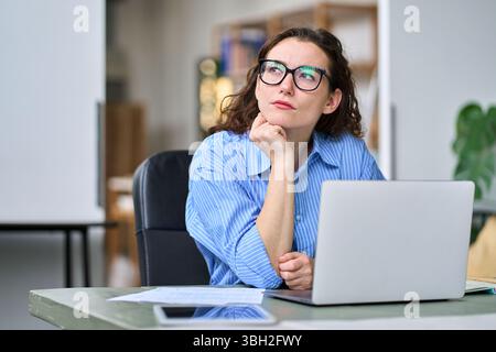 Thoughtful serious professional woman using laptop, looking away thinking. Stock Photo