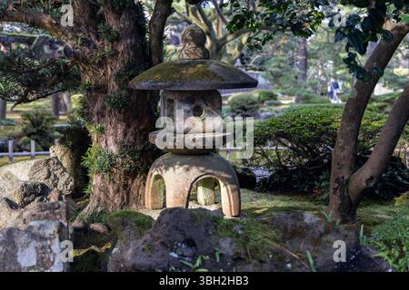 Traditional Japanese stone lantern surrounded by moss-covered rocks and trees in a landscaped garden setting with natural daylight and rich textures Stock Photo