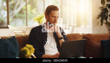 Man, website and reading on sofa with laptop, writer and thinking for script draft in home. Person, editor and technology in living room for research Stock Photo