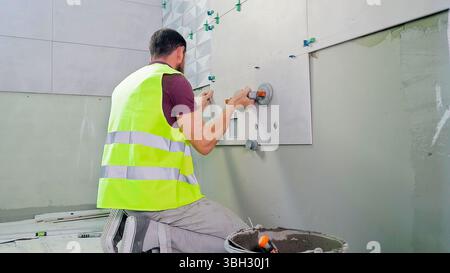 Construction Worker Installing Wall Tiles with Suction Tool. Back view of a construction worker in a safety vest installing large wall tiles using Stock Photo