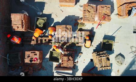 Construction workers laying bricks on a building site. A top-down view of construction workers in high-visibility gear laying bricks at a building Stock Photo