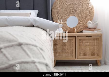 Bedside table with mirror, decor and books near bed indoors Stock Photo