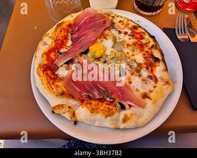 Thin‑Crust Pizza with Prosciutto, Mushrooms and Cheese on Restaurant Table Stock Photo