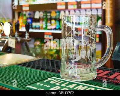Empty, foamy beer mug on a bar counter in a pub, with blurred bottles and taps in the background. Stock Photo