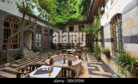 A tranquil courtyard with traditional Middle Eastern architecture, featuring a central fountain, arched windows, and lush greenery. Tables with drinks Stock Photo